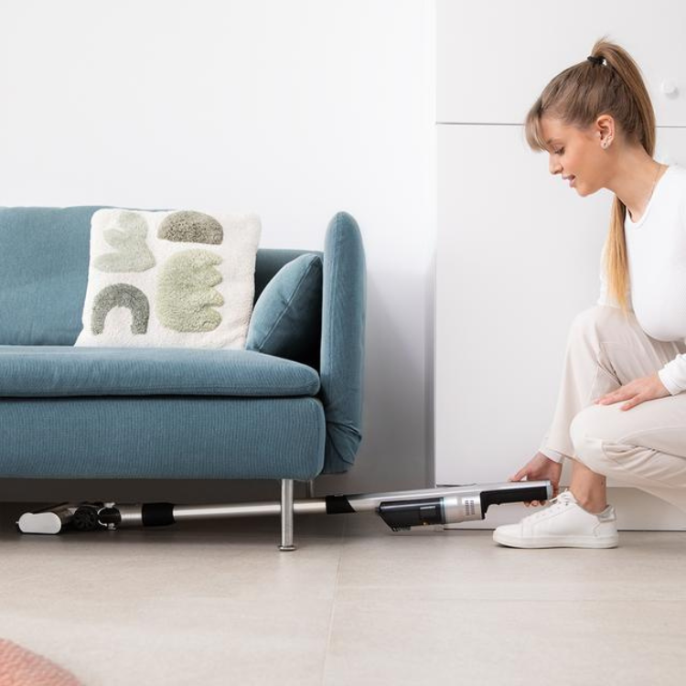 Woman using Cecotec Scoba 2100 Jalisco vacuum under couch.