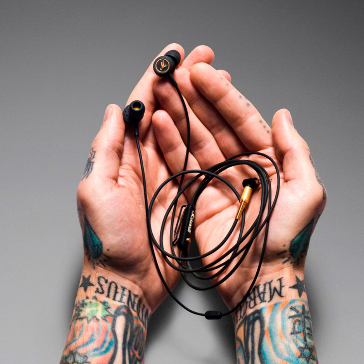 Auriculares Marshall Mode EQ preto enrolados em mãos com tatuagens.