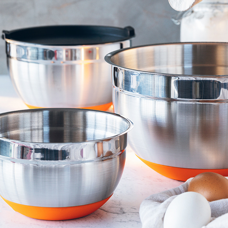 Stainless steel bowl set with orange bases, 3 sizes, with eggs and mixer in background.