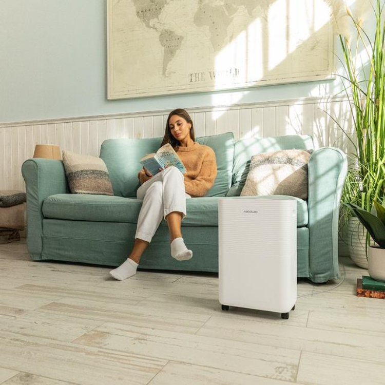 Cecotec BigDry dehumidifier, white, next to a couch with a woman reading.