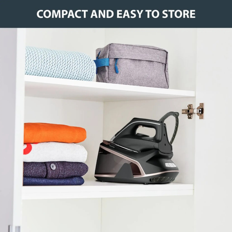Black and rose gold Rowenta iron on shelf with folded clothes.