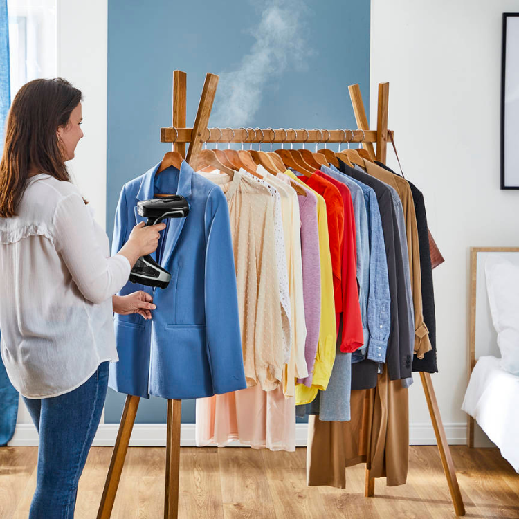 Woman steaming blue jacket on rack with Rowenta steam iron.