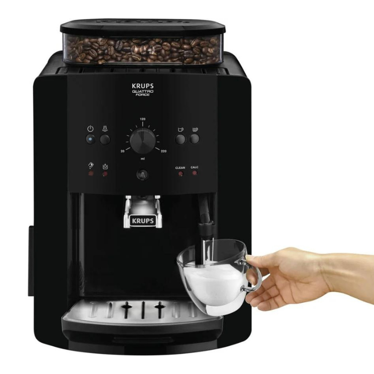 Black Krups espresso machine with coffee beans, hand holding cup under spout.