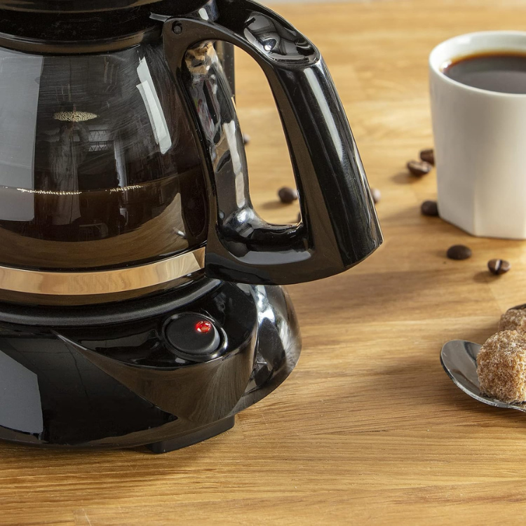 Black Moulinex coffee filter machine on wooden table with cup and coffee beans.