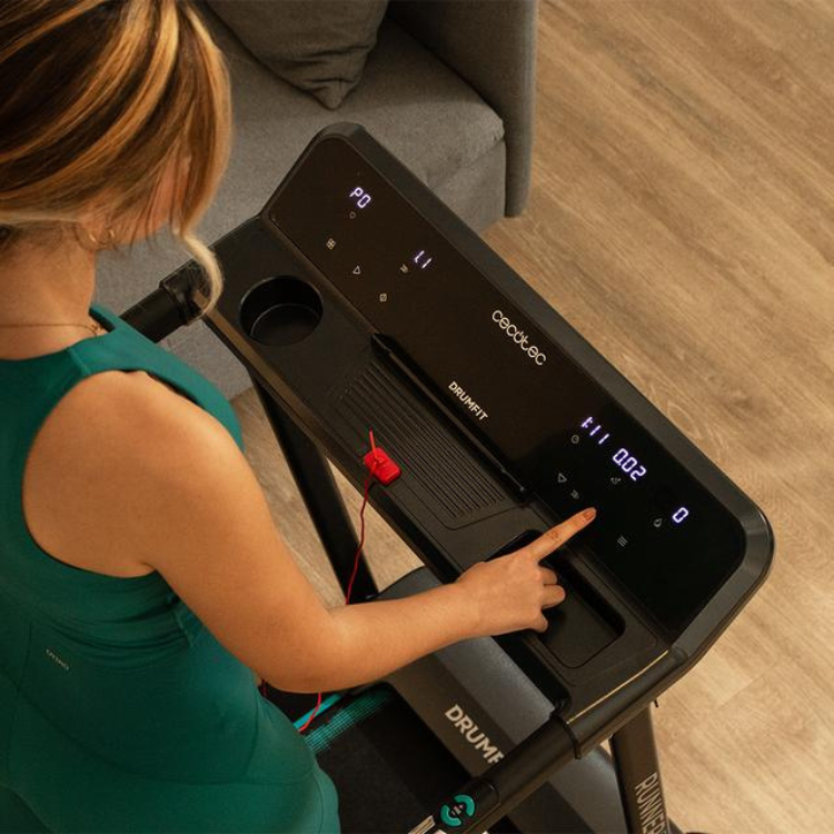 Woman in green dress using Cecotec DrumFit WayHome 1000 Runner Sprint black treadmill.