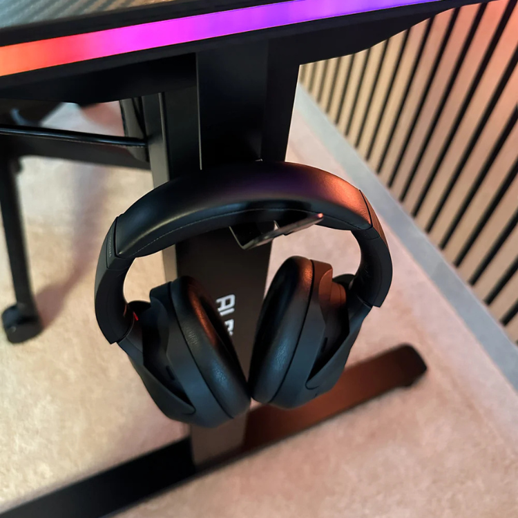 Black gaming headset on stand under desk with RGB lights, white logo.