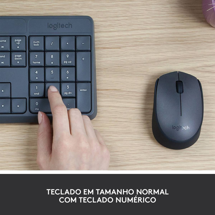 Logitech MK235 wireless keyboard and mouse set, black, on a wooden desk with a hand pressing a key.