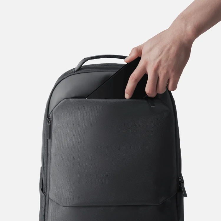 Mochila Xiaomi Business Backpack 15,6" preta, com alça e bolsos laterais, sendo segurada por uma mão por cima.