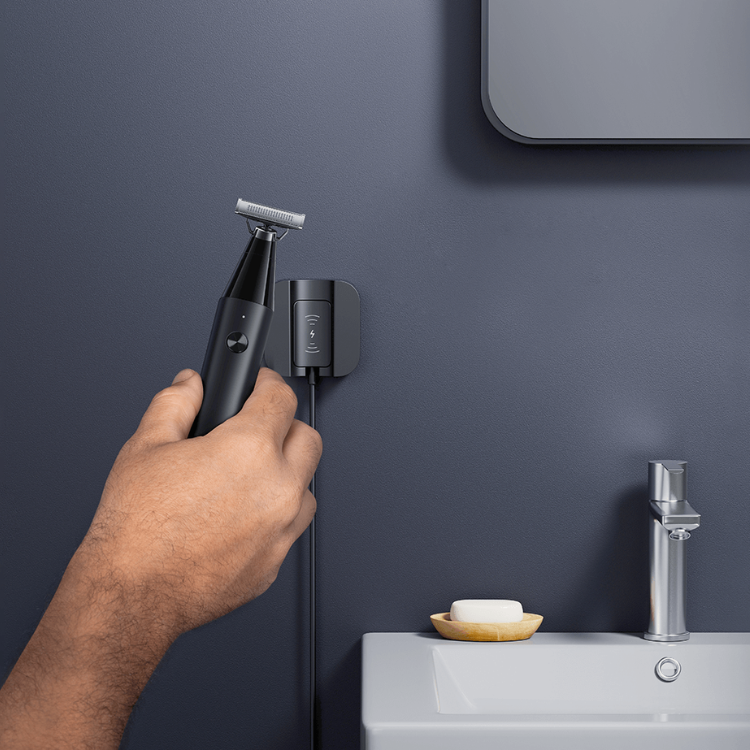Black Xiaomi Uniblade Trimmer with silver blade, hand holding it, on bathroom sink with soap and faucet.